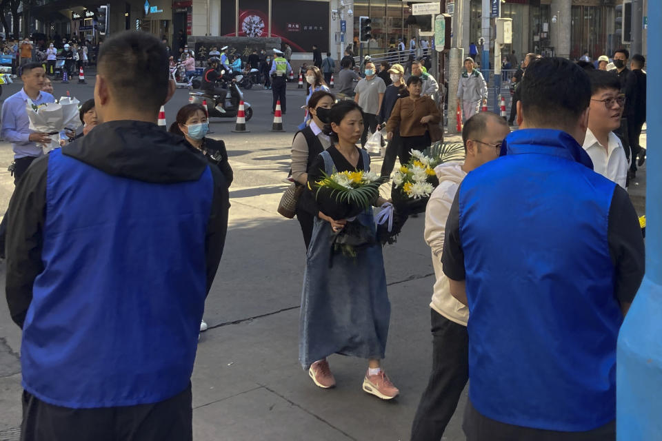 Security personnel in blue vest stand watch as residents with flowers head to a residential building where the late Chinese Premier Li Keqiang spent his childhood in Hefei city, in central China's Anhui province, Thursday, Nov. 2, 2023. Hundreds, possibly thousands, of people gathered near a state funeral home Thursday as former Premier Li Keqiang was being put to rest. (AP Photo/Ken Moritsugu)