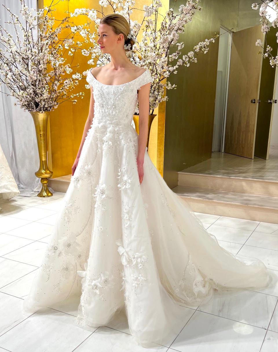 A woman poses in an off-the-shoulder wedding dress with floral applique.