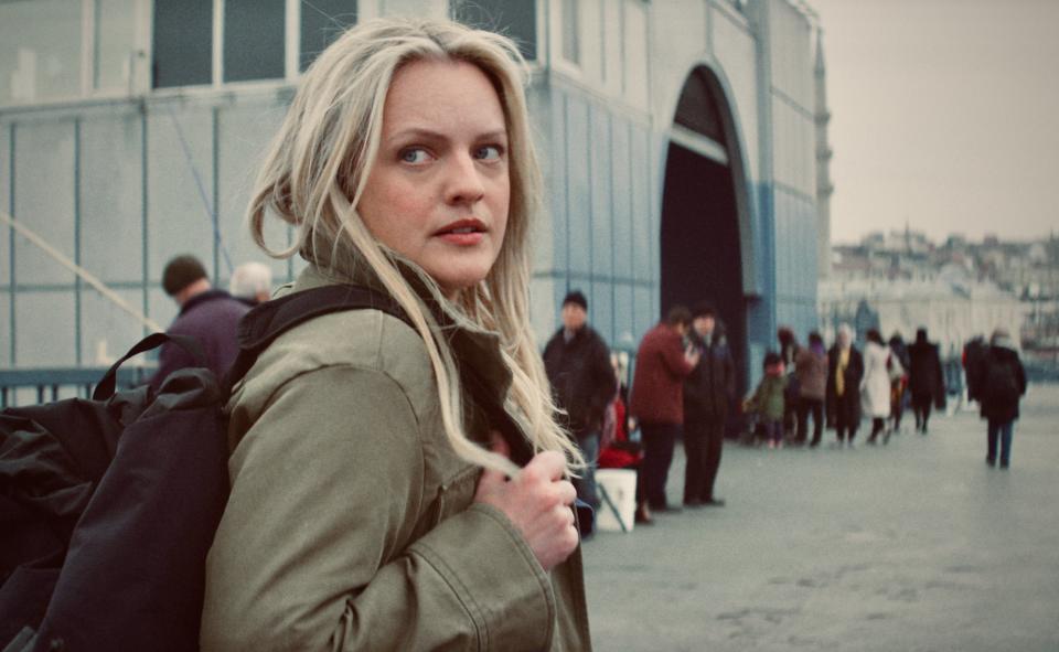 Elisabeth Moss in a scene, looking over shoulder with concerned expression, people in background in The Veil