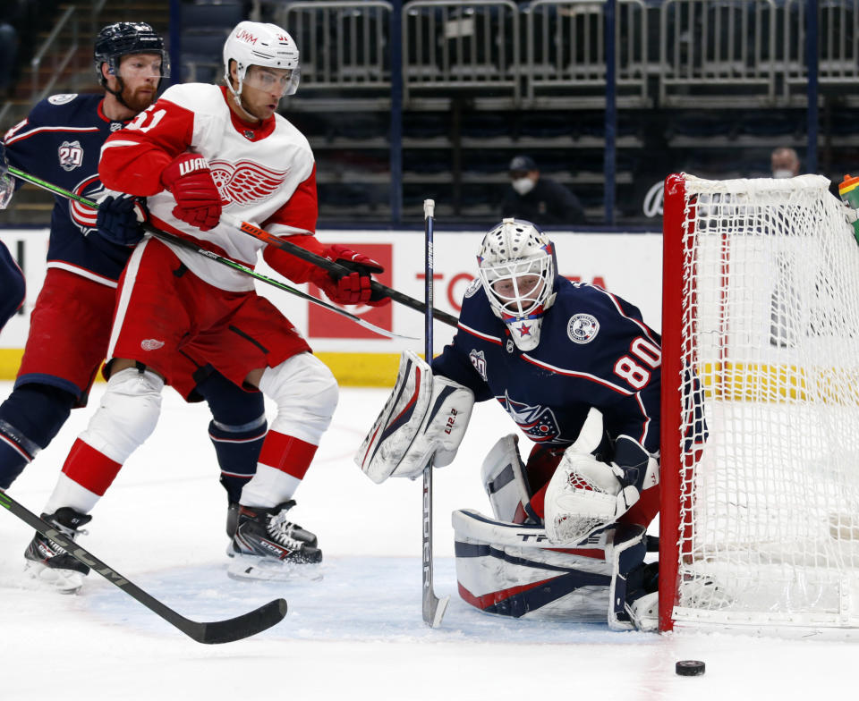 THIS CORRECTS THAT KIVLENIEKS DIED OF CHEST TRAUMA FROM AN ERRANT FIREWORKS MORTAR BLAST AND NOT A SUBSEQUENT FALL AS AUTHORITIES PREVIOUSLY REPORTED - FILE - Columbus Blue Jackets goalie Matiss Kivlenieks, right, stops a shot in front of Detroit Red Wings forward Valtteri Filppula, center, and Blue Jackets defenseman Vladislav Gavrikov during the first period of an NHL hockey game in Columbus, Ohio, in this Saturday, May 8, 2021, file photo. The Columbus Blue Jackets and Latvian Hockey Federation said Monday, July 5, 2021, that 24-year-old goaltender Matiss Kivlenieks has died. A medical examiner in Michigan says an autopsy has determined that Columbus Blue Jackets goaltender Matiss Kivlenieks died of chest trauma from an errant fireworks mortar blast, and not a fall as authorities previously reported. Police in Novi, Michigan, said the mortar-style firework tilted slightly and started to fire toward people nearby Sunday night, July 4. (AP Photo/Paul Vernon, File)