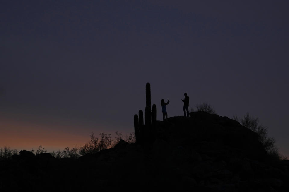 A couple takes photos at dusk, Sunday, July 30, 2023, in Phoenix. Phoenix hit its 31st consecutive day of at least 110 degrees Fahrenheit (43.3 Celsius). The National Weather Service said the temperature climbed to a high of 111 Fahrenheit before the day was through. (AP Photo/Matt York)