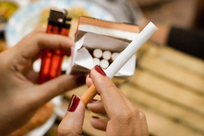 Person's hand with red nails holding a cigarette and a box of matches