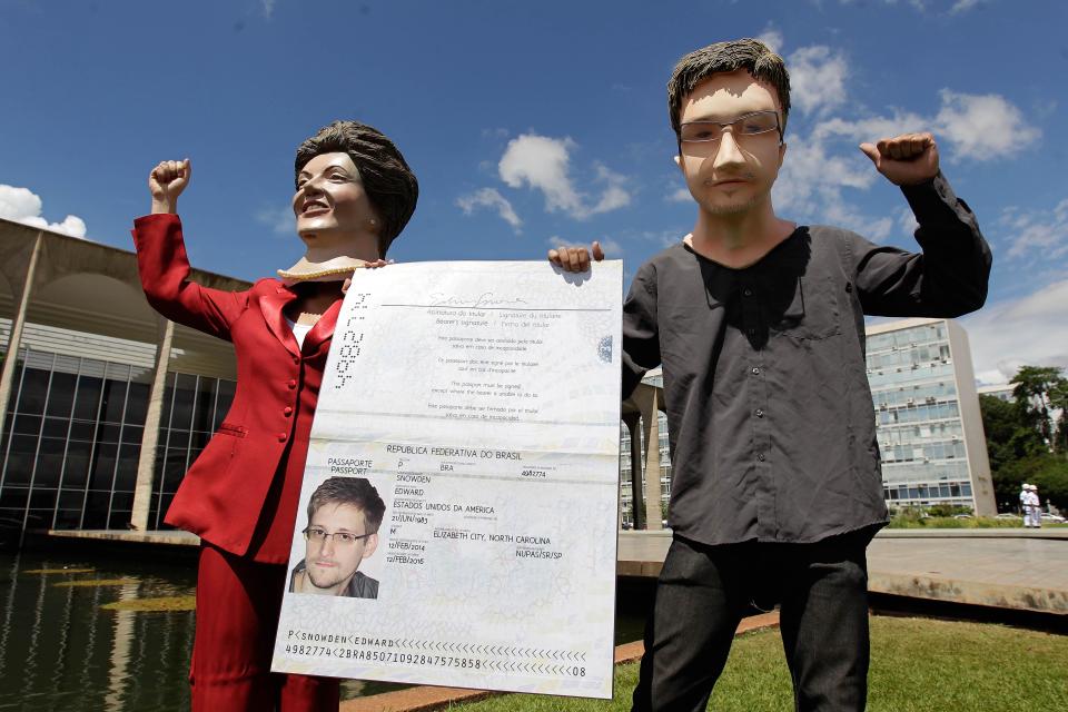 Activistas con máscaras que representan a la presidenta brasileña Dilma Rousseff, izquierda, y al exanalista estadounidense de inteligencia Edward Snowden sostienen una pancarta que imita el pasaporte de Snowden en las afueras del ministerio de Relaciones Exteriores en Brasilia, Brasil, el jueves 13 de febrero de 2014. Activistas y actores entregaron en la cancillería una petición con más de un millón de firmas para que Brasil le conceda asilo al exanalista norteamericano. (AP Photo/Eraldo Peres)