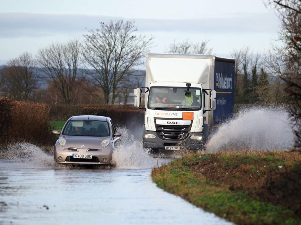 Vehicles driven through a flooded road in Aldingbourne, West Sussex last week (PA)