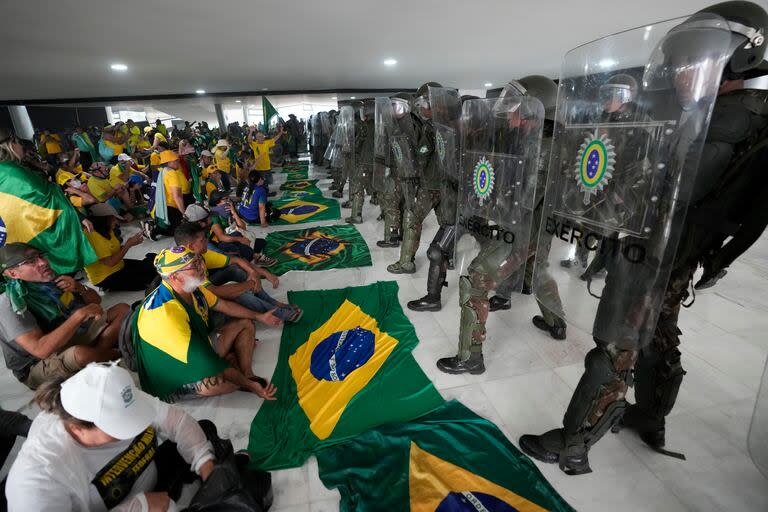 Simpatizantes del expresidente brasileño Jair Bolsonaro permanecen sentados frente a una hilera de policías militares dentro del Palacio de Planalto, luego del asalto vandálico del 8 de enero de 2023