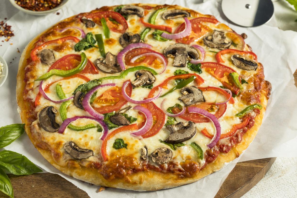 A picture of a homemade veggie pizza with mushrooms, peppers, tomatoes and spinach.