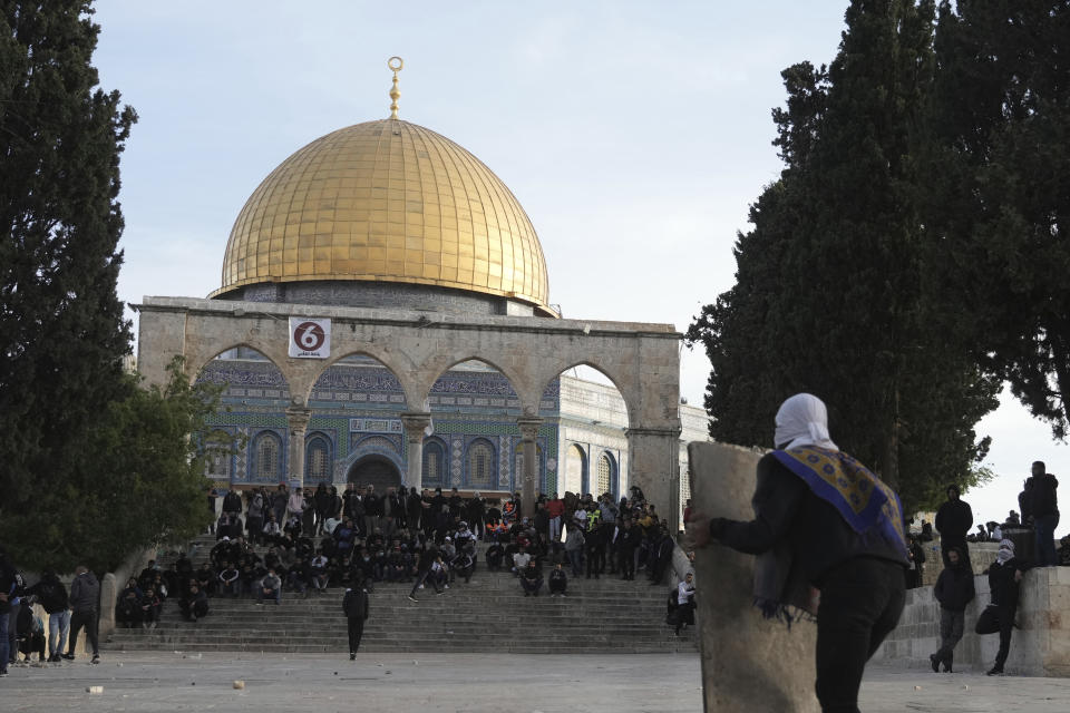 A Palestinian protester takes cover behind a makeshift shield during clashes with Israeli police at the Al Aqsa Mosque compound in Jerusalem's Old City, Friday, April 22, 2022. Israeli police and Palestinian youths clashed again at a major Jerusalem holy site sacred to Jews and Muslims on Friday despite a temporary halt to Jewish visits to the site, which are seen as a provocation by the Palestinians. (AP Photo/Mahmoud Illean)