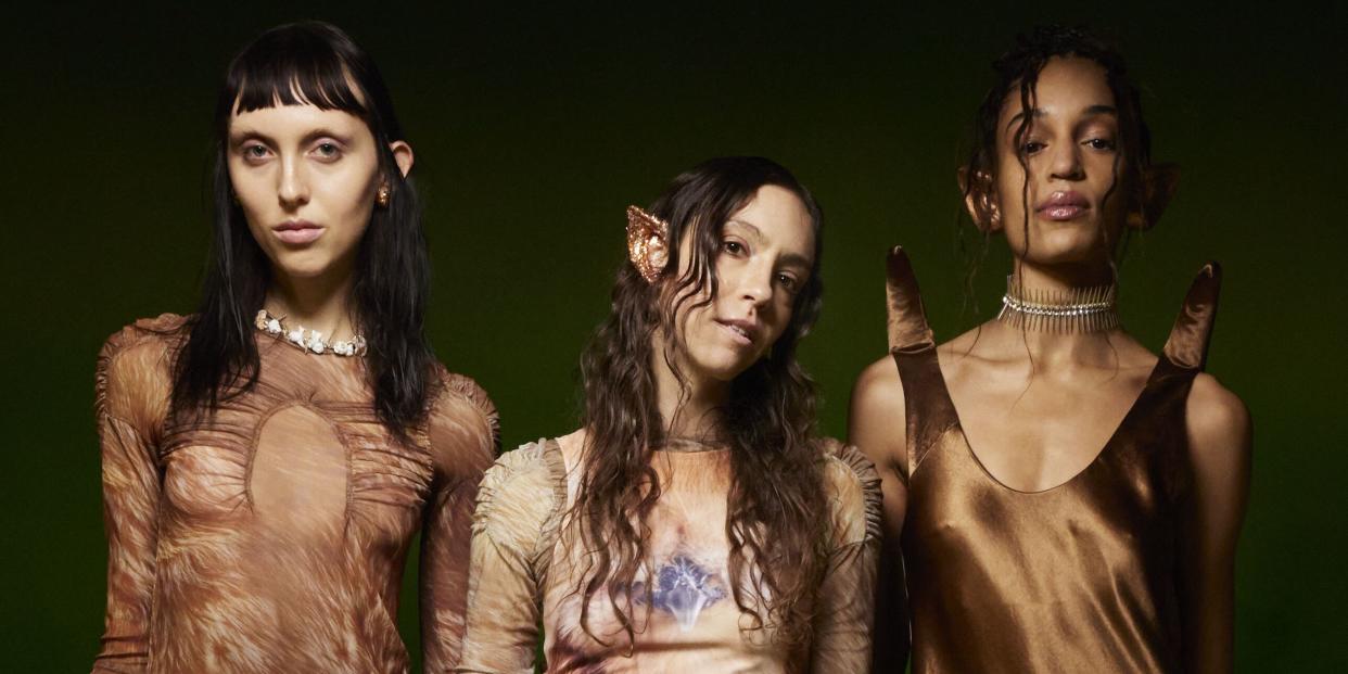 designer hillary taymour of collina strada, wearing brown tie dye and elf ears, stands backstage with two models at her fall 2023 show