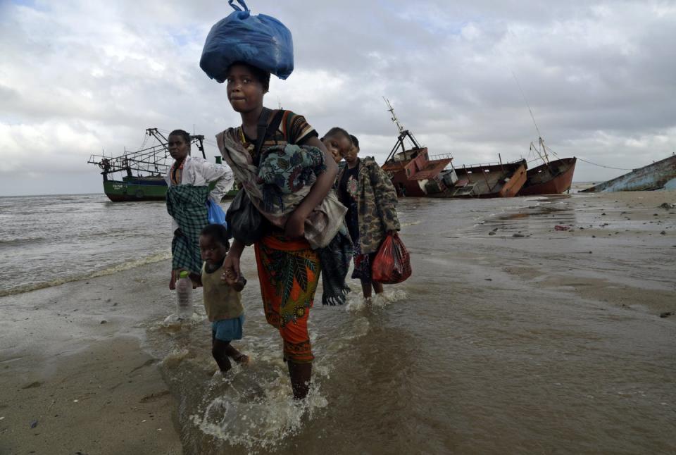 People walk along a beach with bags on their heads and belongins in their arms after being rescued from a flooded area