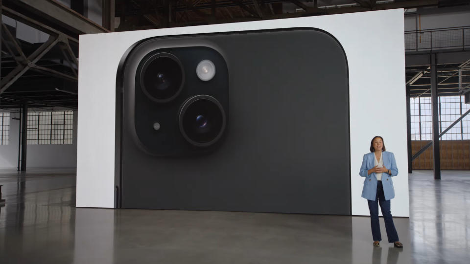 The black Apple iPhone 15 on a screen in a warehouse with a person stood in front