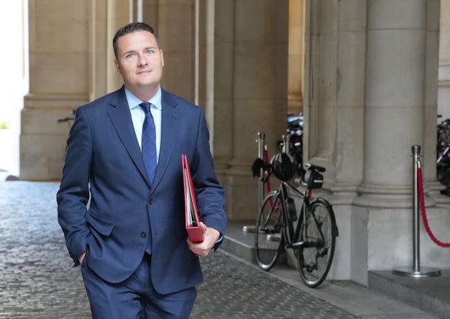 Wes Streeting wearing a suit and holding a red Government folder under his arm