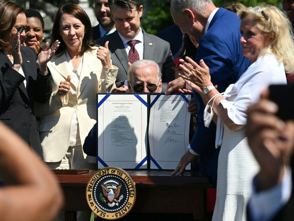 President Joe Biden holds up the signed CHIPS Act while surrounded by onlookers