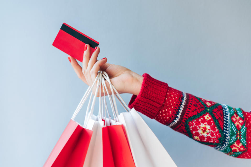 Frau mit roter Kreditkarte in der Hand, Weihnachtspullover und Shopping-Taschen in der Hand