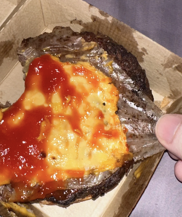 Hand holding a cardboard takeaway box with a cheese-smothered steak topped with sauce