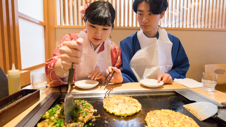 A man and woman cooking okonomiyaki at their table