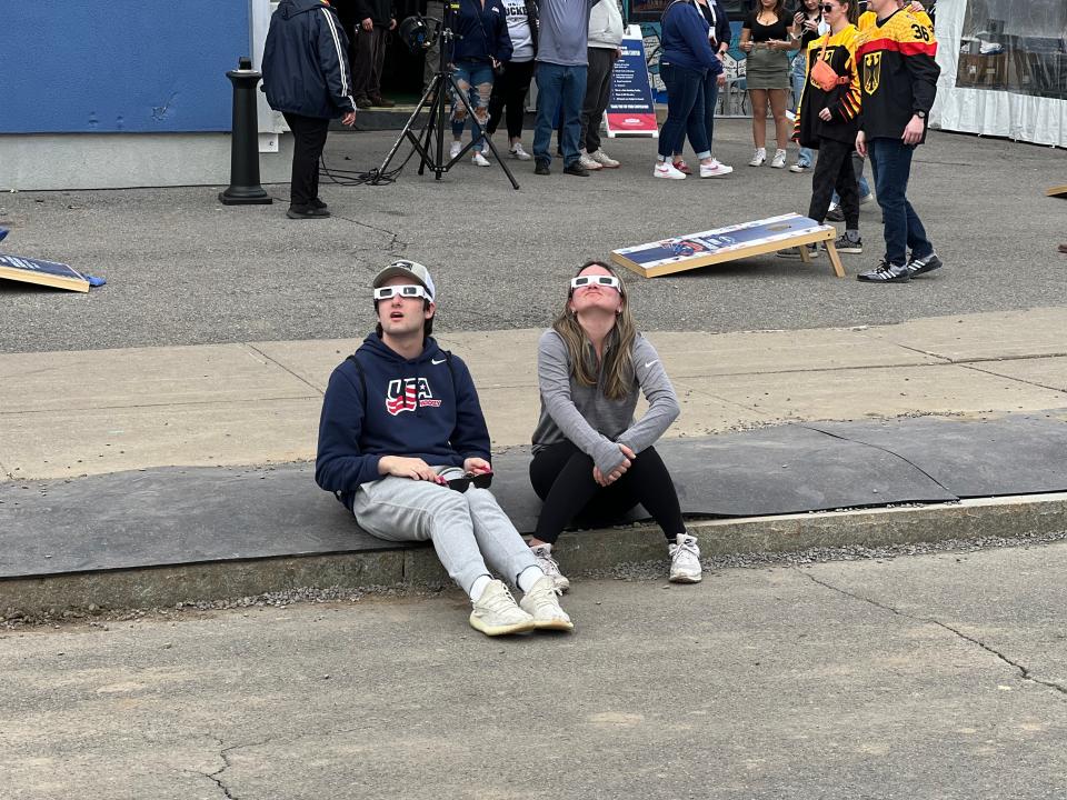 An out-of-town couple takes a look at the sky with eclipse glasses at the Subaru World Championship Village, outside the Adirondack Bank Center, which is hosting the IIHF Women's World Championship in Utica, on Monday, April 8, 2024.