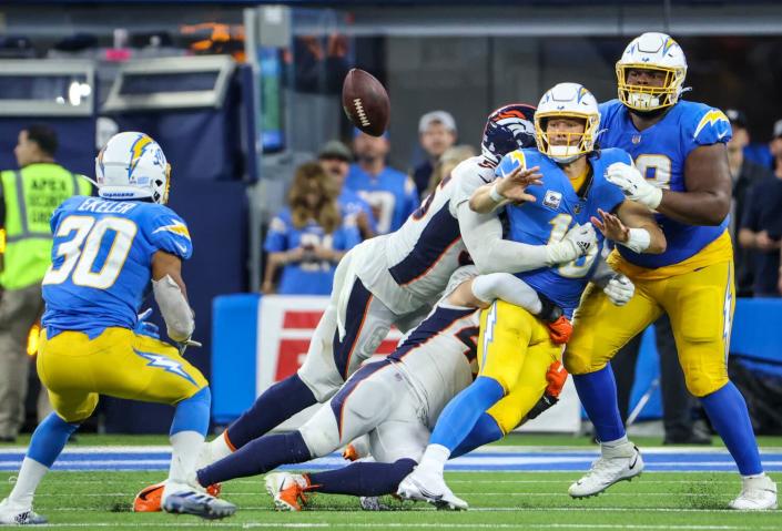 The Chargers' Justin Herbert (10) flips a pass to Austin Ekeler (30) as he is tackled late in the game against the Broncos.