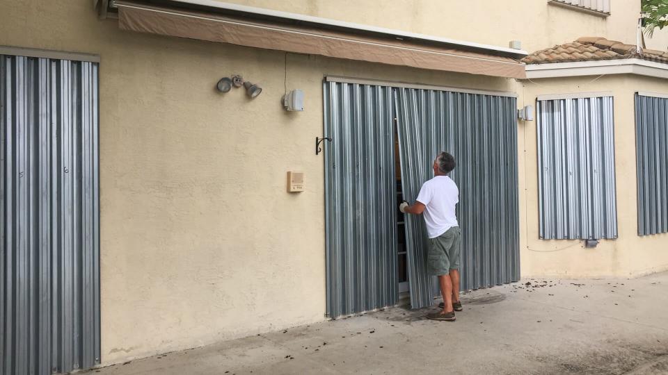 Man installing hurricane metal shutters on house door, Miramar, Florida, USA.