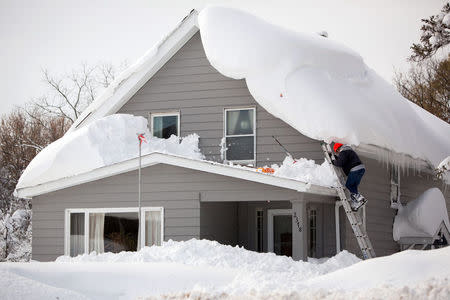 A man climbs on his roof to clear snow in the town of Cheektowaga near Buffalo, New York, November 19, 2014. REUTERS/Lindsay DeDario