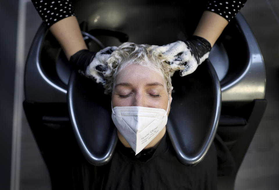 Hairdresser Jule Napiontek washes the hair of her customer Sophie Pilgrim wearing a face mask in the 'Salon Success' in Magdeburg, Germany, Monday, March 1, 2021. Hairdressers across Germany have reopened for business this morning after a more than 2-month closure, another cautious step as the country balances a desire to loosen restrictions with concern about the impact of more contagious coronavirus variants. (Ronny Hartmann/dpa via AP)