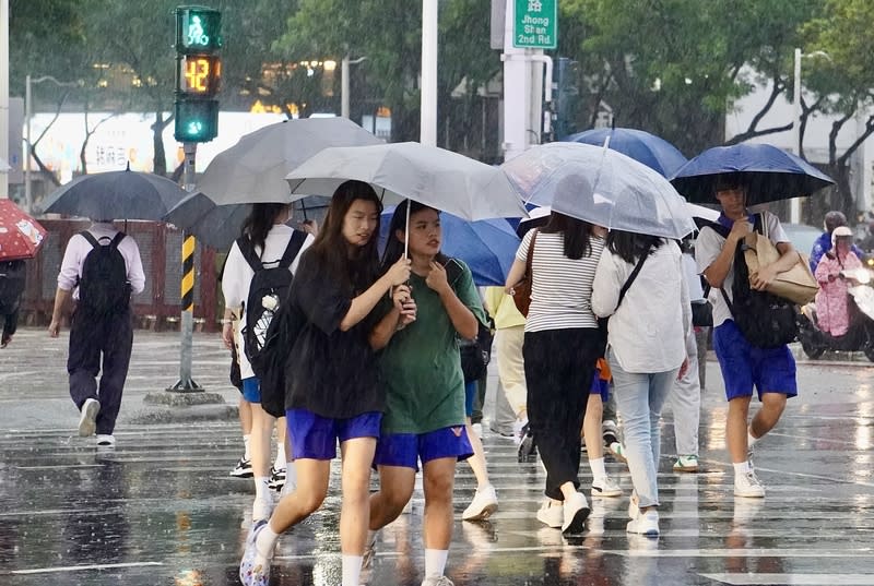 鋒面通過，中央氣象署24日提醒易有短延時強降雨發 生，下午並持續針對高雄等縣市發布大雨特報。圖為高雄市新興區傍晚出現雨勢，街頭民眾撐傘過馬路。（中央社）