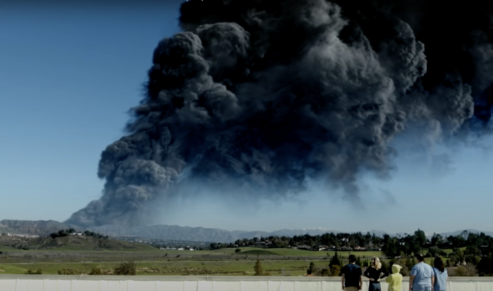 A large cloud of black smoke in the sky while five onlookers watch