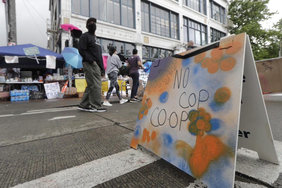 People walk near what is being called the "No Cop Co-op" were protesters and others can get free food and other supplies, Thursday, June 11, 2020, inside what is being called the "Capitol Hill Autonomous Zone" in Seattle. Following days of violent confrontations with protesters, police in Seattle have largely withdrawn from the neighborhood, and protesters have created a festival-like scene that has President Donald Trump fuming. (AP Photo/Ted S. Warren)