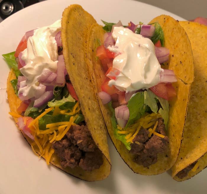 Two tacos with beef, cheese, lettuce, tomato, onions, and sour cream