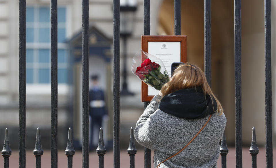 A woman reads the official death notice of Britain's Prince Philip as she prepares to lay flowers at the gate of Buckingham Palace in London, Friday, April 9, 2021. Buckingham Palace officials say Prince Philip, the husband of Queen Elizabeth II, has died. He was 99. (AP Photo/Alastair Grant)