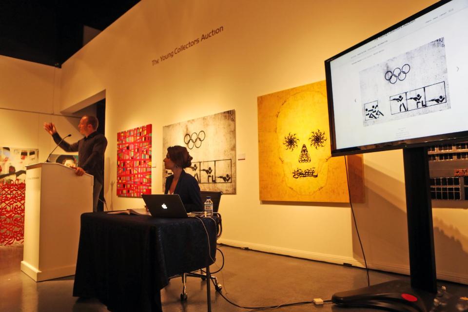 In this Monday, Sept. 16, 2013 photo, auctioneer Hisham Samawi, left, auctions a piece by the Syrian artist Tammam Azzam, titled "Syrian Olympic," which appears on the monitor, right, during an auction at Ayyam gallery, that moved from Damascus to Dubai in late 2011, in Dubai, United Arab Emirates. The auction Monday in Dubai's evolving art district served as a window into a small but forward-looking effort to save one niche of Syria's artistic community with no end in sight to the civil war that has already claimed more than 100,000 lives. (AP Photo/Kamran Jebreili)