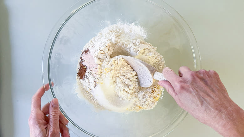 Stirring flour, sugar, spices, and lemon zest in bowl with wooden spoon