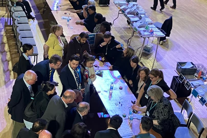 Candidates for Oldham East and Saddleworth gather around a counting table to verify doubtful ballots.