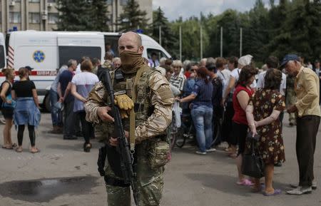 An armed man stands guard as people wait for humanitarian medical aid near the mayor's office in Slaviansk July 9, 2014. REUTERS/Gleb Garanich
