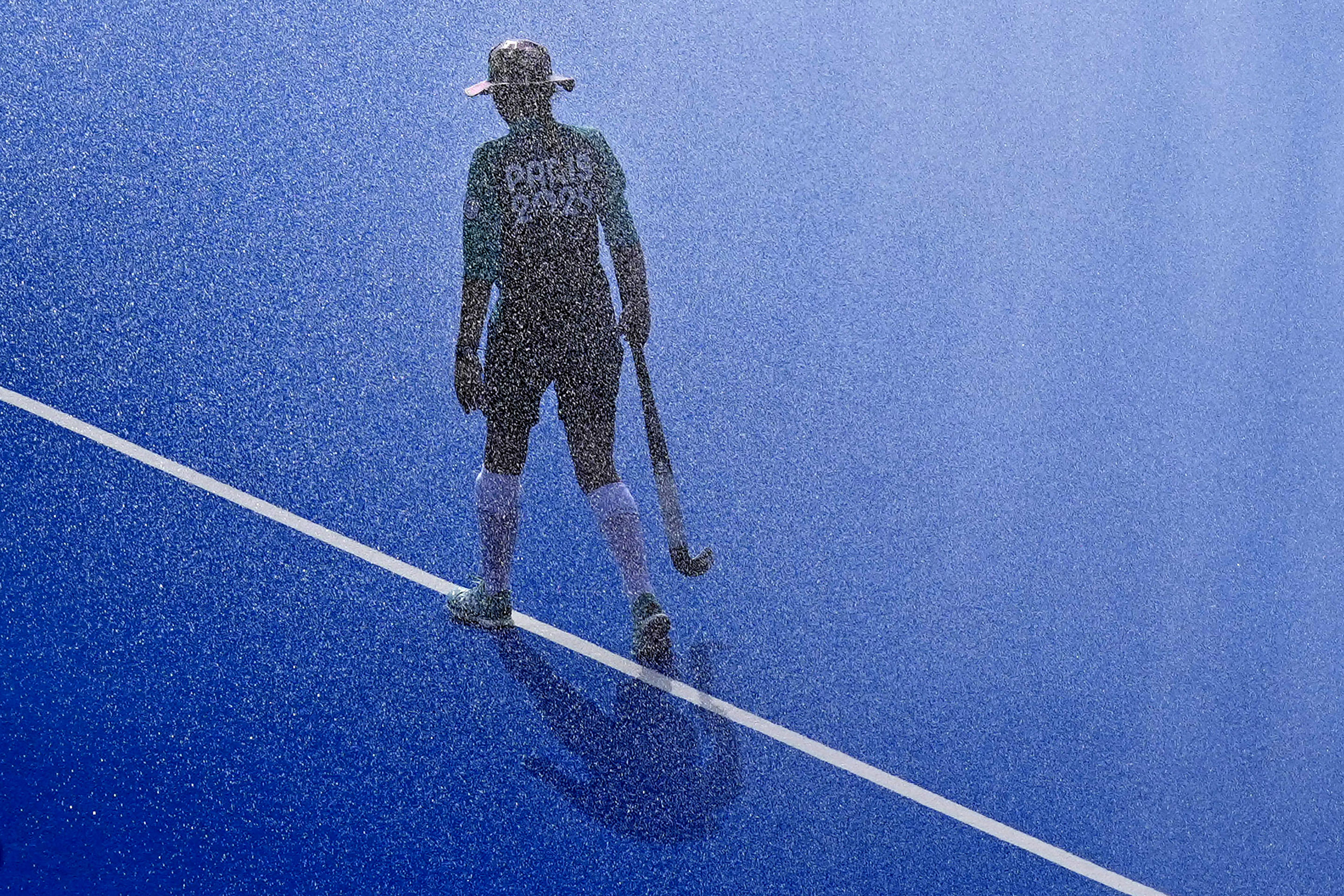 Water is sprayed on the pitch as a ball girl walks along the center line before the start of the men's Group A field hockey match between South Africa and Germany at the Yves-du-Manoir Stadium during the 2024 Summer Olympics on July 30, 2024, in Colombes, France. (Aijaz Rahi/AP)