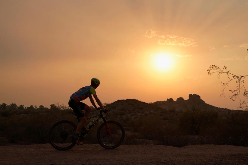 A cyclist bikes past the setting sun at Papago Park during a heat wave where temperatures hit 115 degrees on June 15, 2021, in Phoenix.