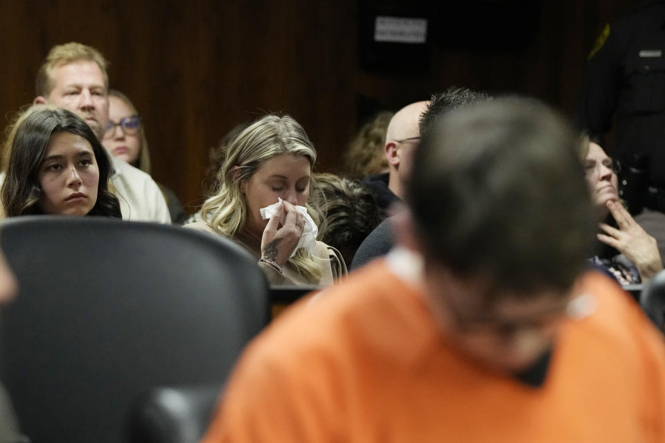 Ethan Crumbly, foreground, looks downward as victim family members listen to impact statements, Friday, Dec. 8, 2023, in Pontiac, Mich. Crumbly was sentenced to life in prison for killing four students, wounding more and terrorizing Michigan's Oxford High School in 2021. A judge Friday rejected pleas for a shorter sentence and ensured that Crumbley, 17, will not get an opportunity for parole. (AP Photo/Carlos Osorio)