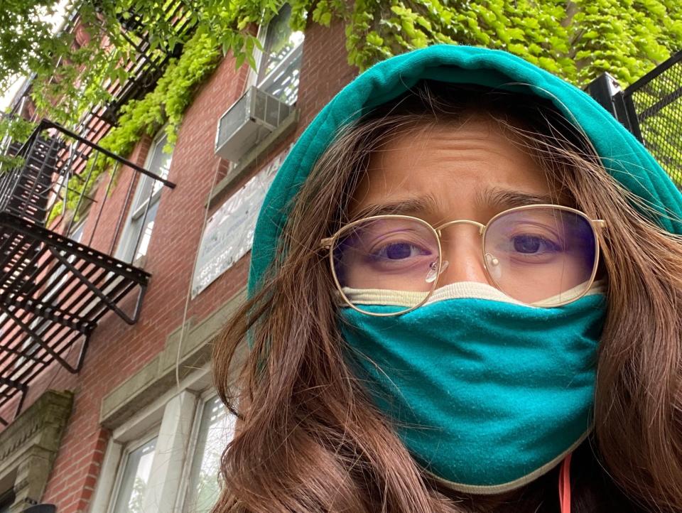 The author is seen in front of her Brooklyn apartment wearing a turquoise hoodie and mask