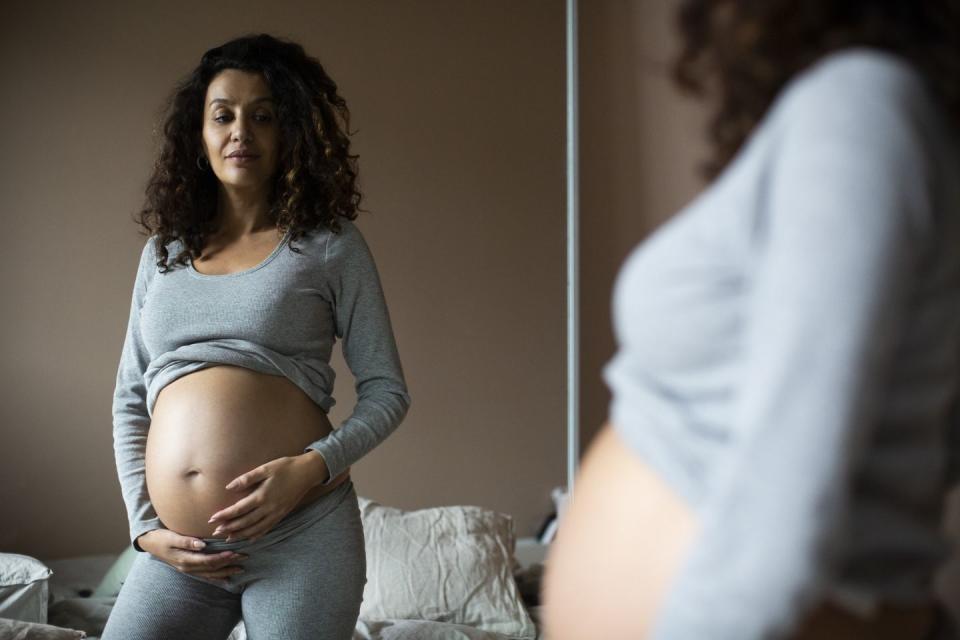 pregnant woman looking in mirror at her bump while at home