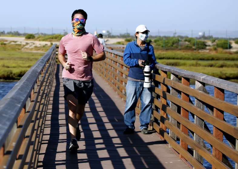 A jogger and a wildlife photographer wear masks as they enjoy the afternoon at Bolsa Chica Ecological Reserve in Huntington Beach, on Wednesday, May 20, 2020.