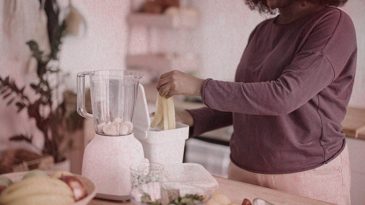 a person standing at a counter juicing, a blender is seen as well