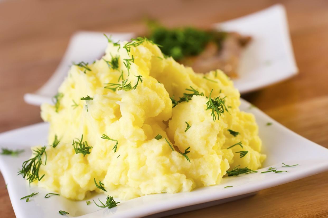 Closeup of mashed potatoes on a white plate with a blurred background of a white plate of salmon, all on a wooden table