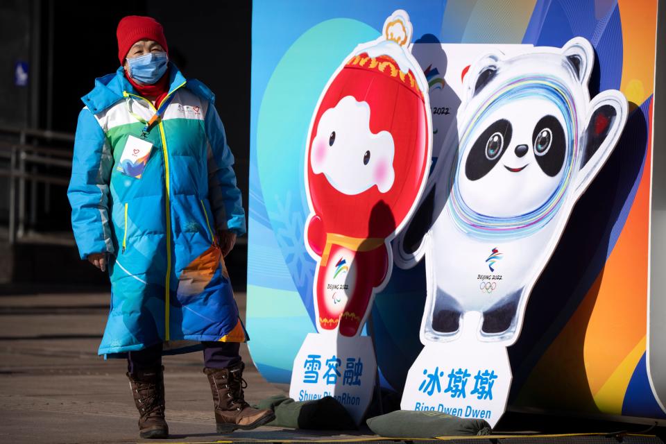 A woman wearing a face mask to protect against COVID-19 stands next to figures of the Paralympic and Olympic mascots in Beijing, Saturday, Jan. 15, 2022.