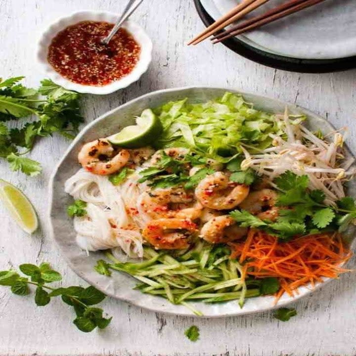 A bowl with rice noodles, shrimp, and julienned veggies with homemade dressing on the side.