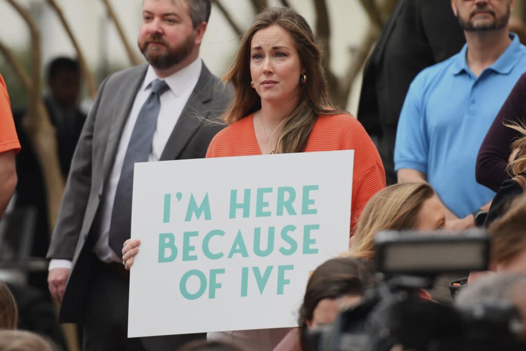 A woman holding a sign saying "I'm Here Because of IVF"
