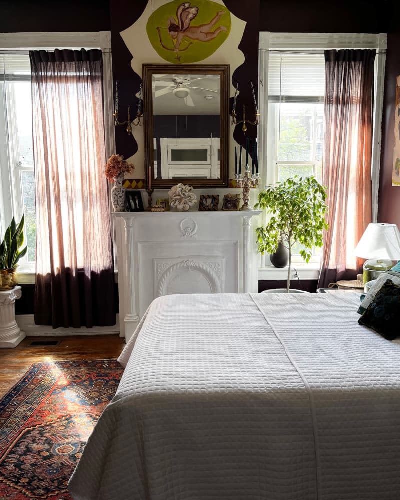 Mirror hangs above white mantel in eggplant bedroom with white bedding.