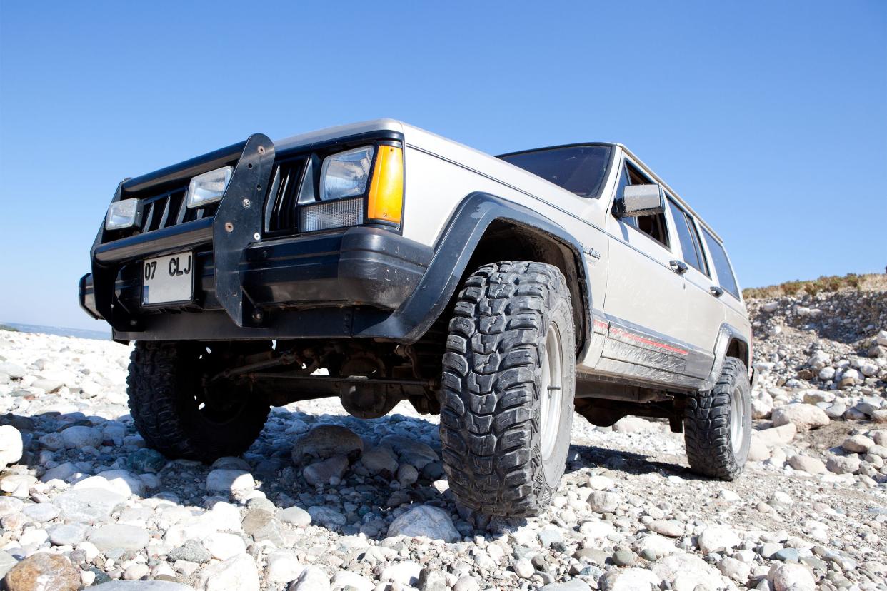 Close up of a beige Jeep Cherokee Sport on a stony beach on a clear sunny day.