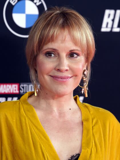 A woman with bangs and dangling earrings in a mustard yellow dress