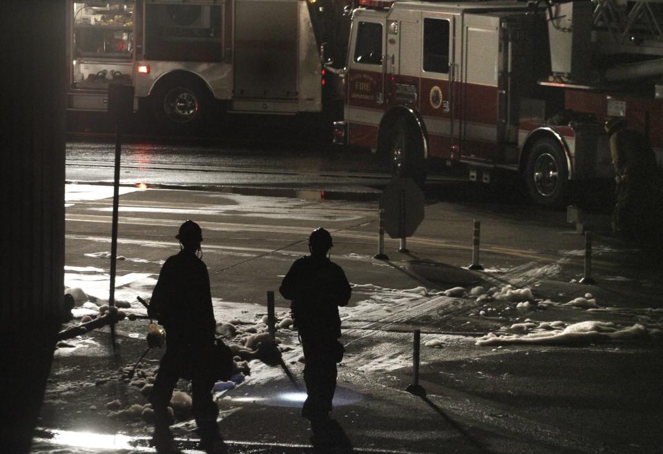 Firefighters carry equipment through foam sprayed on a fire that erupted after a twin-jet Cessna Citation crashed into a hangar after landing at Santa Monica Airport in Santa Monica