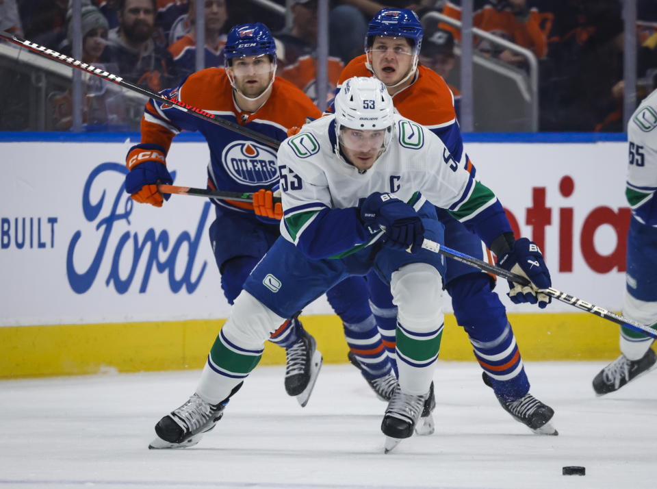 Vancouver Canucks forward Bo Horvat, center, is chased by Edmonton Oilers defenseman Markus Niemelainen, left, and forward Mattias Janmark during first-period NHL hockey game action in Edmonton, Alberta, Friday, Dec. 23, 2022. (Jeff McIntosh/The Canadian Press via AP)