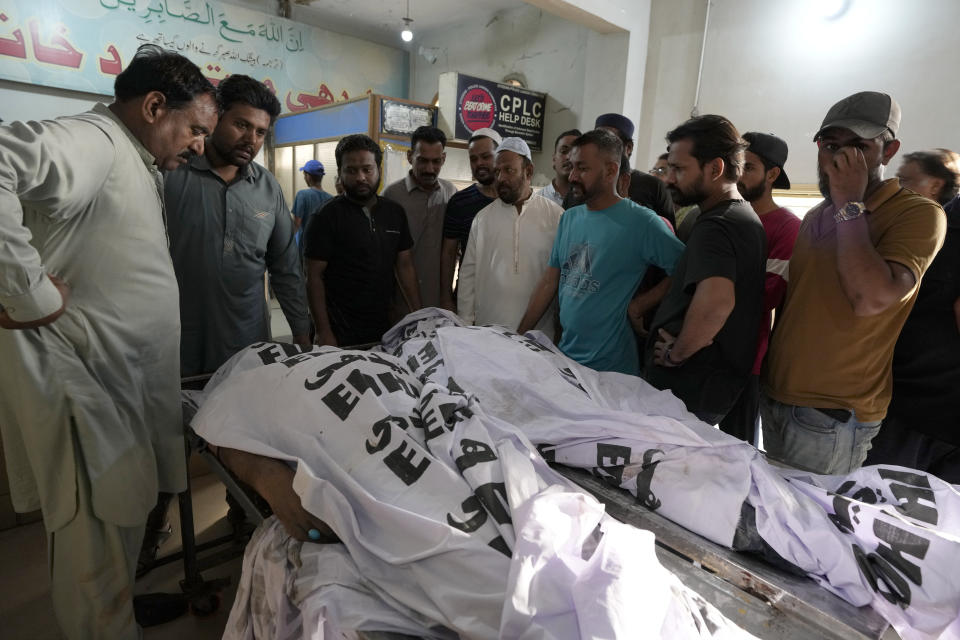 Relatives and others gather around the bodies of fire fighters who died in a fire, at a morgue, in Karachi, Pakistan, Thursday, April 13, 2023. A massive fire broke out in a garment factory in the southern Pakistan port city of Karachi. The cause of the blaze, which ripped through the factory Wednesday night and eventually caused it to collapse, was not immediately known, rescue officials and police said. (AP Photo/Fareed Khan)